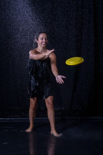 A woman with wet hair and a black dress catching a frisbee in the rain