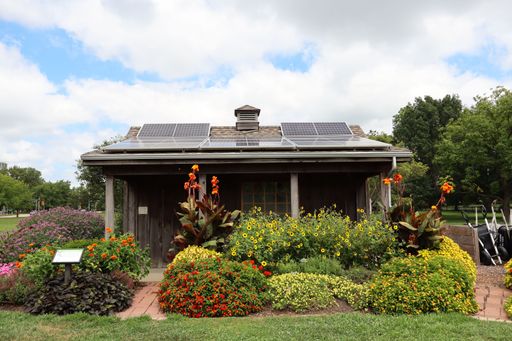 A shed with solar panels surrounded by colorful flowers at a garden.