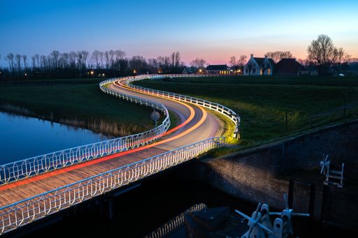 A long exposure shot on the bridge with houses and a silhouette of trees during sunset