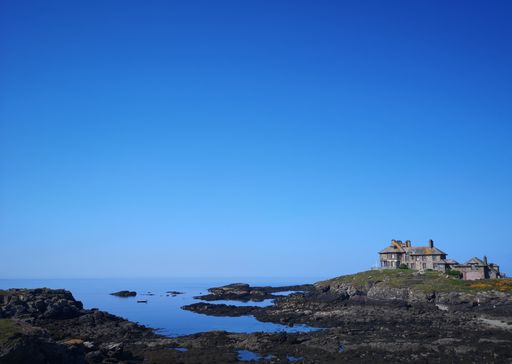 An eerie scenery of an abandoned old building on the shore of a lake with a clear blue sky