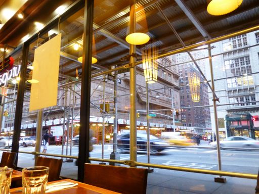 A wide shot of the inside of a cafe with glass windows with the view of the street and cars near buildings