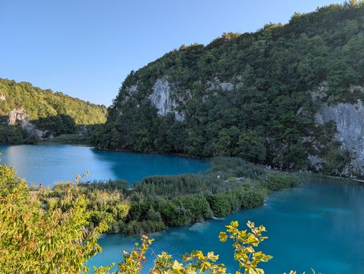 Scenic view of Plitvice Lakes with clear turquoise water and lush green forest under a bright blue sky.