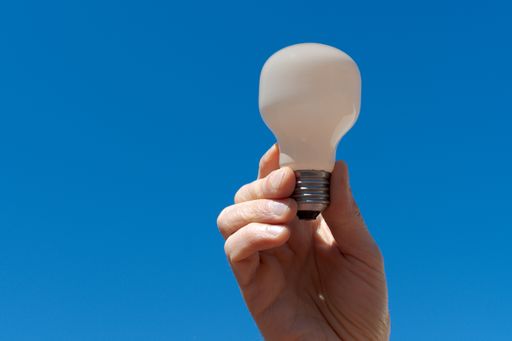 A hand holding an electric bulb with a blue sky in the background