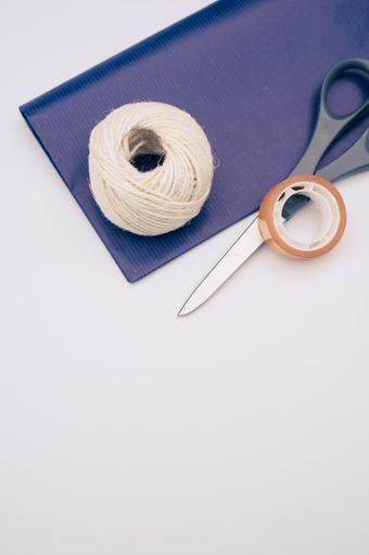 decorative yarn balls with blue paper sheet scissors and tape on a white surface