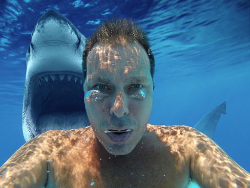 A man taking a selfie underwater with a shark in the background