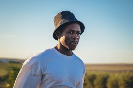 A portrait of a young black handsome man wearing a bucket hat walking along the highway at sunset