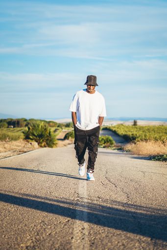 A full body shot of a young black handsome man wearing a bucket hat walking along the highway, sunset