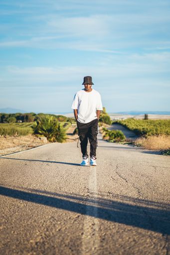 A full body shot of a young black handsome man wearing a bucket hat walking along the highway, sunset