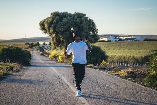 A full body shot of a young black handsome man wearing a bucket hat walking along the highway, sunset