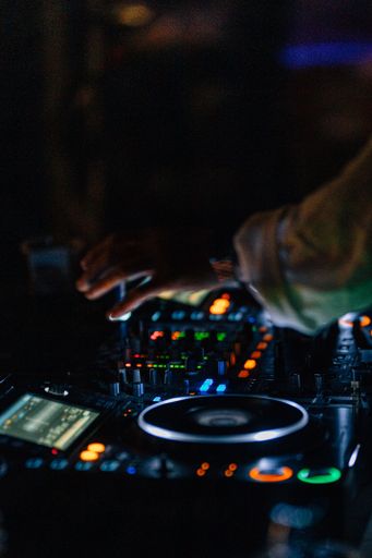 A closeup shot of a DJ hand on a colorful music mixer desk table during a night beach party