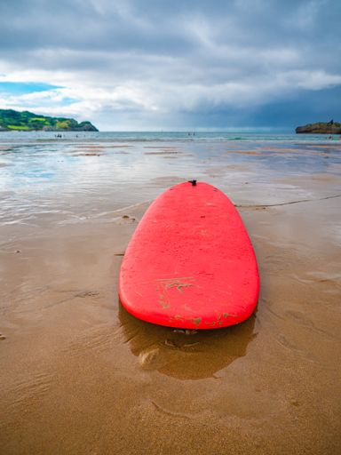 A red surfing board on the sandy beach under a cloudy sky