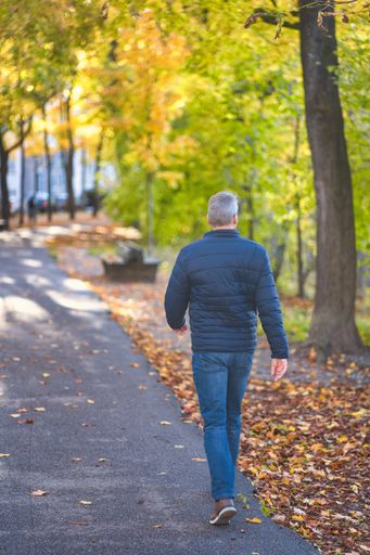 A vertical shot of a lonely man walking on fall streets in autumn weather.