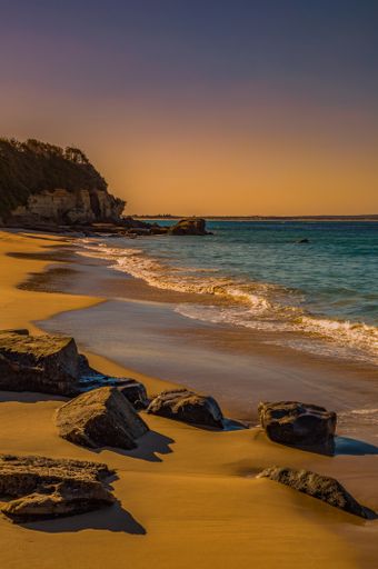 The beautiful sandy coast with rocks around and the sea with cliffs in the background