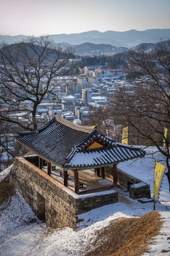 A beautiful view of an outside benches in the snow with mountains and buildings in South Korea