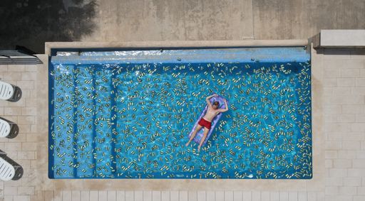 A bird's eye view of a pool full of beer cans and a man floating on an inflatable mattress