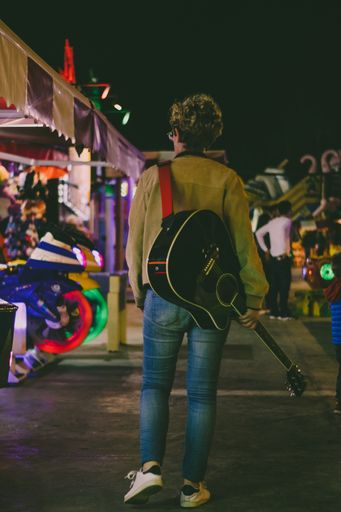 A vertical shot of a man with a guitar in a stree