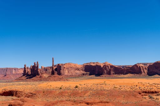 A scenic view of Monument Valley's red rock formations under a clear blue sky, showcasing the iconic desert landscape.