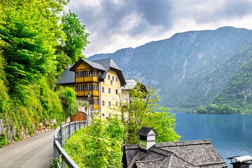 Scenic view of a charming yellow house by a lake with lush greenery and mountains in Hallstatt, Austria.