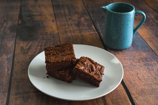 Warm chocolate brownies on a white plate and a blue mug on a wooden table