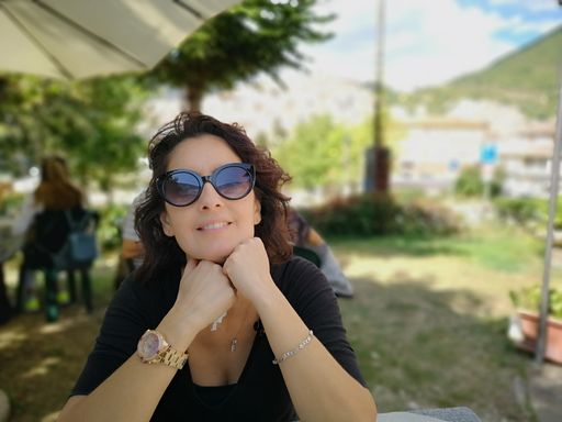 A smiling Italian woman wearing sunglasses with hands under her face