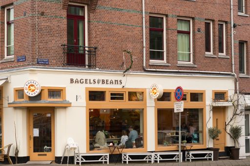 Front entrance of a Bagels and Beans restaurant with people sitting inside in the city center.