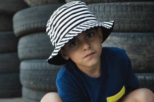 A portrait of a cute little Caucasian boy wearing a hat on the background of old car tires