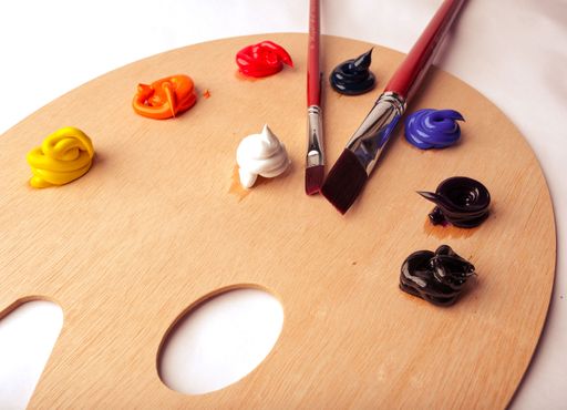 Colorful artist palette with brushes and vibrant paint dabs on a wooden surface, showcasing creativity and art supplies.