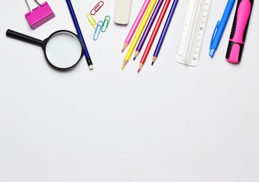 A top view of stationery isolated on a white background. The magnifying glass, pencils, markers, ruler and clips