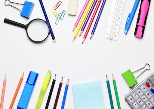 A top view of stationery isolated on a white background. The magnifying glass, calculator, pencils, markers, ruler, and clips