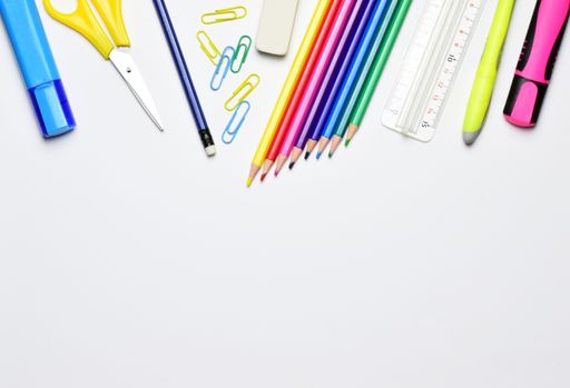 A top view of stationery isolated on a white background. The scissors, pencils, markers, ruler, and clips