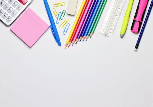 A top view of stationery isolated on a white background. The pencils, markers, papers, calculator, ruler, and clips