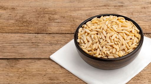 A bowl of uncooked orzo pasta placed on a wooden table with a white napkin underneath, showcasing its texture and color.