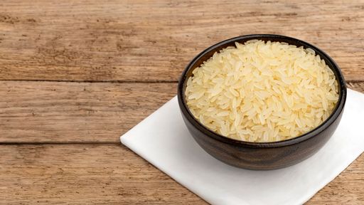 A wooden bowl filled with uncooked rice on a white napkin atop a rustic wooden table, showcasing a simple culinary setup.