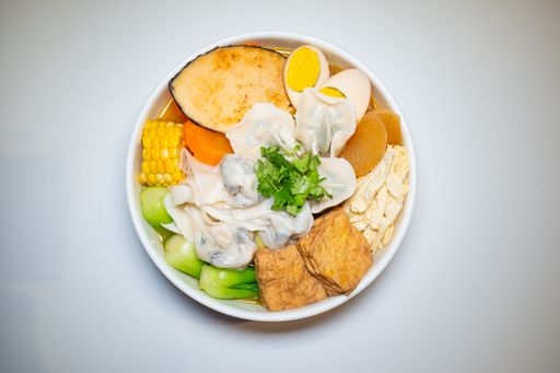 A vibrant bowl of Asian noodle soup with vegetables, tofu, egg, and dumplings, garnished with cilantro, on a white background.