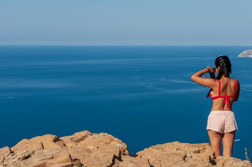 An East Asian woman from her back on a cliff in Provence, France, looking at the sea