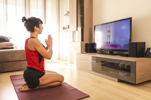A young brunette doing exercises at home in the covid19 quarantine, raising her arms while watching TV