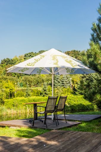 A vertical shot of a beautiful garden with a table with a white umbrella, and chairs