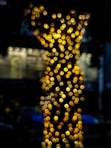 A vertical shot of a blurry tree stem with many yellow bokeh lights around