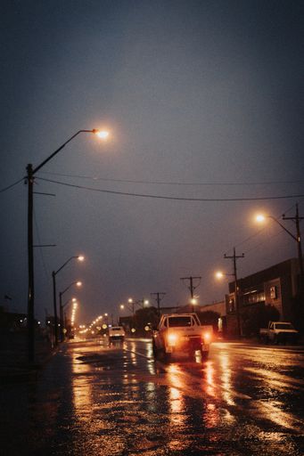 A vertical shot of the wet road with cars at night.