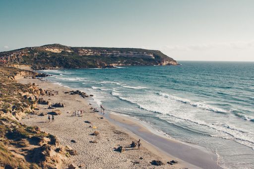 A wide shot of a cliff by the sandy seashore under a clear sky