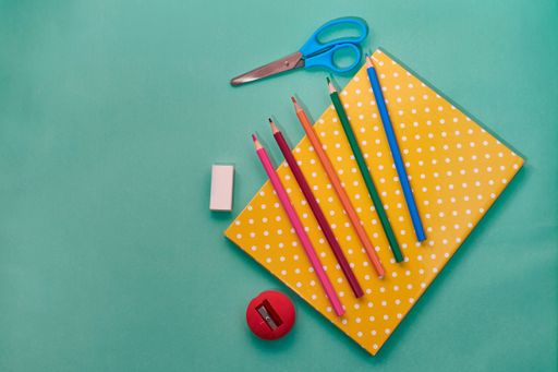 A top view shot of a notebook, colorful pencils, scissors, and a rubber isolated on a green background