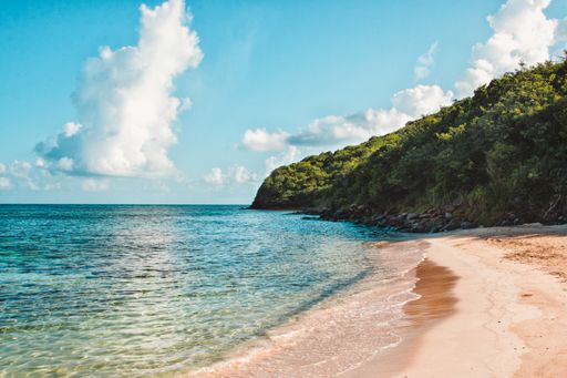 A wide shot of a green cliff by the sea under a clear blue sky with clouds