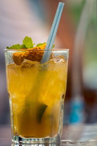 A closeup of a glass of cold cocktail with ice cubes and a straw