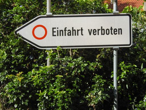 A "No Entrance" signboard in German attached on a pole against green plants