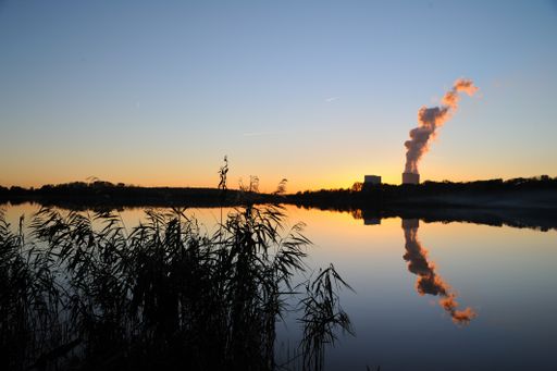A cloud of smoke from the chimney from chemical plant and a reflection of it in a lake at a sunset