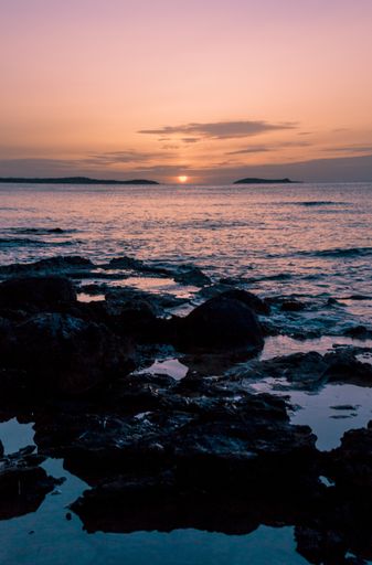 A beautiful vertical shot of a rocky seashore and a sea during the sunset