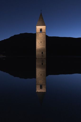 A vertical shot of the stone tower in Reschen Pass, Italy reflecting in the water next to it