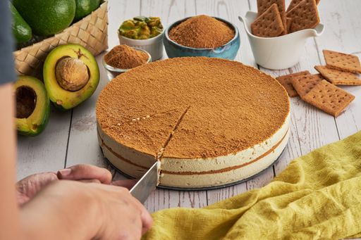A closeup shot of a hand slicing a piece of cake, avocados, and other ingredients