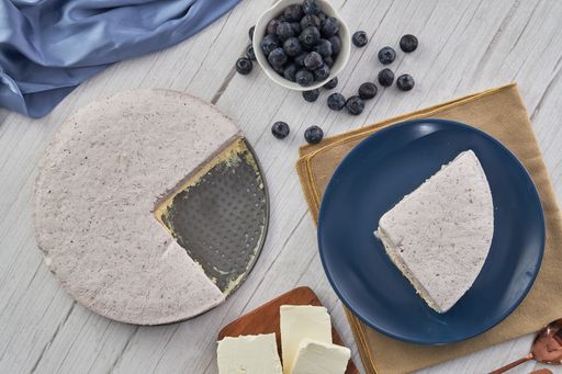 A top view of a sliced blueberry cream cake, berries, and other ingredients