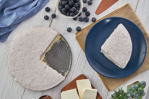 A closeup shot of a sliced blueberry cream cake, berries, and other ingredients